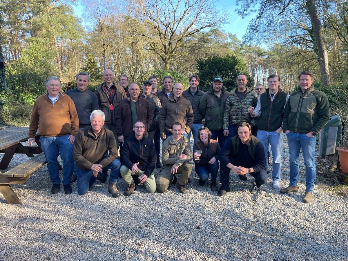 A full cohort of candidates and assessors standing together on the gravel outside the Berkenhorst lodge, in stalking clothing, on a bright day in early spring.